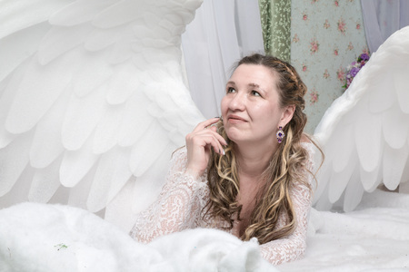 Ugly woman in a white dress with white wings is trying to look as angelの写真素材