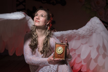 Ugly woman in a white dress with white wings is trying to look as angel