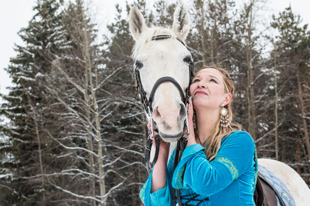Woman in national dress and white horse in a forest in a winter dayの写真素材
