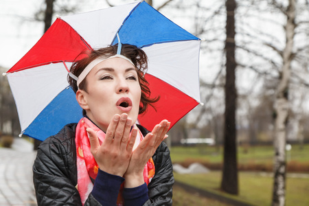Emotional girl with colorful umbrella on her head in the park in a rainy dayの写真素材