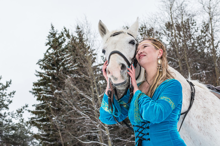 Woman in national dress and white horse in a forest in a winter dayの写真素材