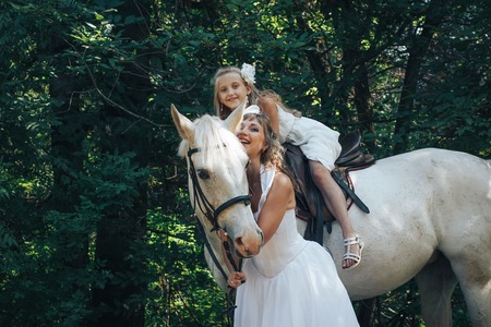 Bride, small girl and white horse in the park in a nice dayの写真素材