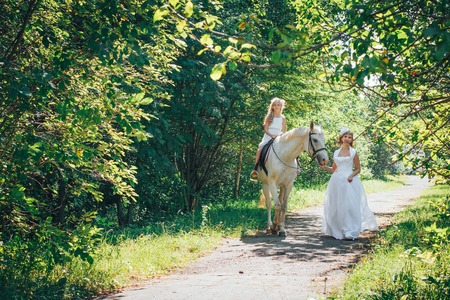 Bride, small girl and white horse in the park in a nice dayの写真素材