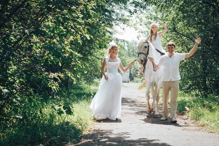 Man, woman dressed as a bride, girl and white horse in the parkの写真素材