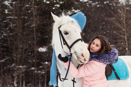 Nice girl and white horse outdoor in snowfall in a winterの写真素材
