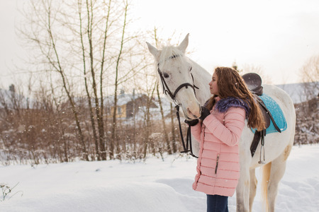 Nice girl and white horse outdoor in snowfall in a winterの写真素材
