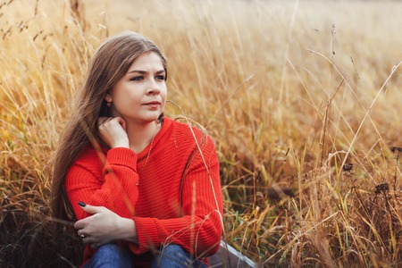 Beautiful girl in red dress in a yellow field in an autumn dayの写真素材