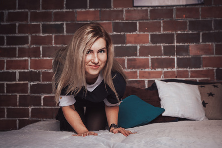 Nice blond girl in black dress on the bed indoorsの写真素材
