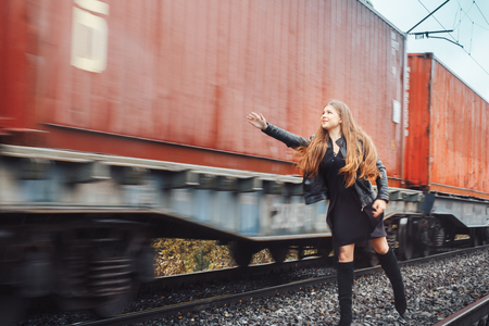 Nice girl in a black dress on a railway road near moving trainの写真素材