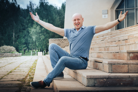 Funny bald man sits on the steps in the Park in a cloudy summer dayの写真素材