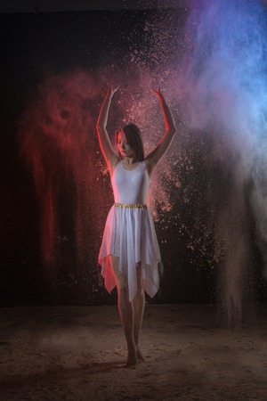 Beautiful slim female dancer in white dress in studio during Powder Photo Shoot with colored light