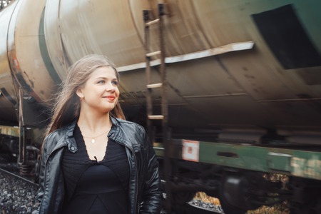 Nice girl in a black dress on a railway road near moving trainの写真素材