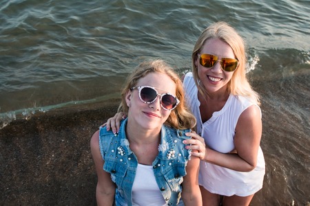 Two blond girls on the beach near sea or ocean. Mother and daughter have fun together