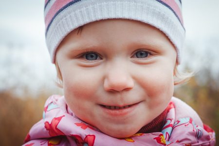 Portrait of a child of a little girl in a warm hat and warm clothes in an autumn dayの写真素材