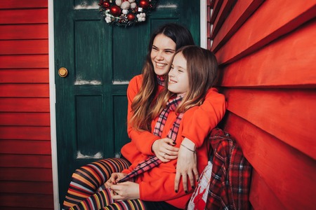 Two girls are sisters in red sweaters and striped scarves relax and have fun in a beautiful room, decorated for Christmas and the New yearの写真素材