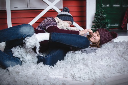 Young couple in sweaters and hats together near red wall of small house decorated for Mary Christmas...