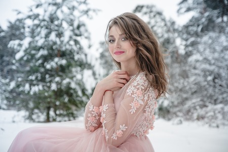 Girl in a beautiful pink dress in a winter forest and snow aroundの写真素材