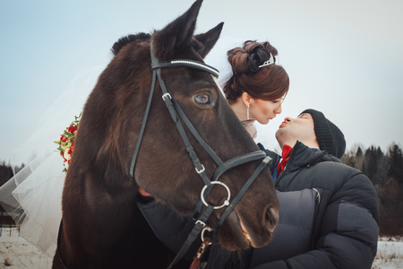 Bride and groom walking with horse near forest in a winter afternoon