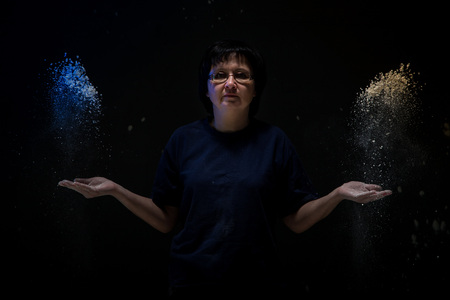 Woman with dark hair in a dark room and flying white powder aroundの写真素材