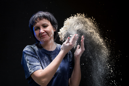 Woman with dark hair in a dark room and flying white powder aroundの写真素材