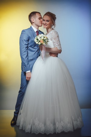 Beautiful bride in a white dress and a young groom in a blue suit in the Studio during a photoshoot with nice lightの写真素材