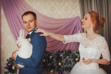 Beautiful bride in a white dress and a young groom in a blue suit indoors in the Studio during a photoshootの写真素材