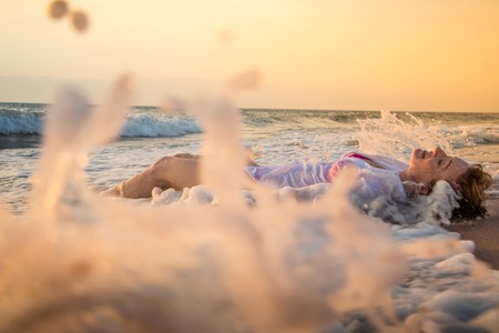 Girl rests and has fun in sea wave at sunset in the eveningの写真素材