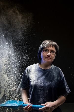 Woman with dark hair in a dark room and flying white powder aroundの写真素材