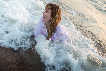 Girl rests and has fun in sea wave at sunset in the eveningの写真素材