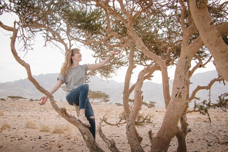 Pretty girl have fun on a tree in the desert in a dayの写真素材