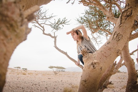 Pretty girl have fun on a tree in the desert in a dayの写真素材