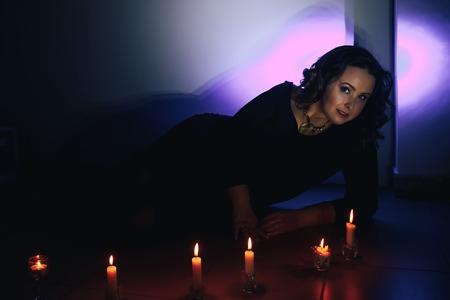 Portrait of fattened girl with black hair and candles in a dark roomの写真素材