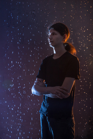Attractive young man in black wet clothes under the rain and splash of water during studio photo shootの写真素材