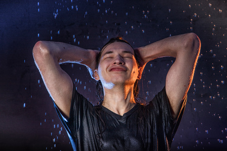 Attractive young man in black wet clothes under the rain and splash of water during studio photo shootの写真素材