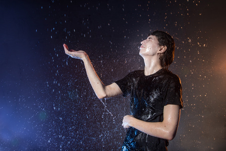 Attractive young man in black wet clothes under the rain and splash of water during studio photo shootの写真素材