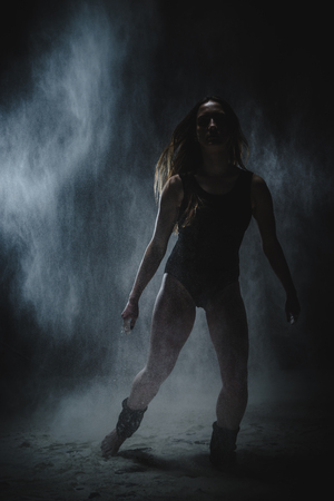 Girl dansing with flour during photoshoot on black backgroundの写真素材