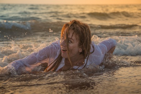Girl rests and has fun in sea wave at sunset in the eveningの写真素材