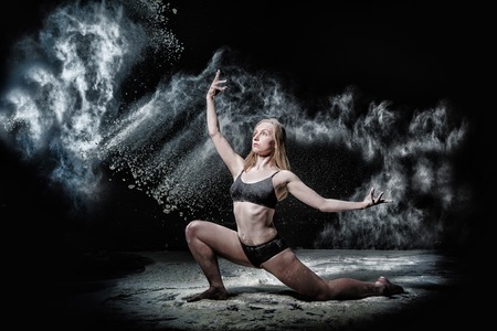 Girl dansing with flour during photoshoot on black backgroundの写真素材
