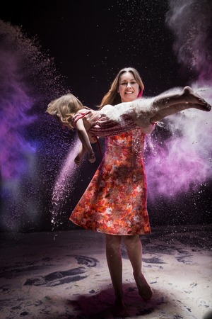 Young mother and small daughter during photoshoot with flour in dark studioの写真素材