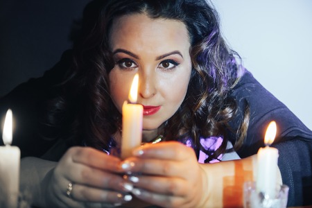 Portrait of fattened girl with black hair and candles in a dark roomの写真素材
