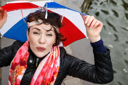 Emotional girl with colorful umbrella on her head in the park in a rainy dayの写真素材