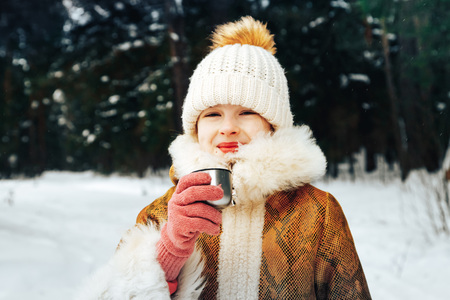 Portrait of a little girl in winter dress in a forest full of snow in a dayの写真素材
