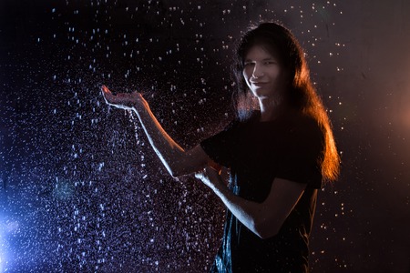 Attractive young man in black wet clothes under the rain and splash of water during studio photo shootの写真素材
