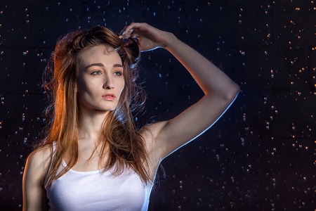 Girl with long hair during photoshoot with water in photo studio and drops of rain behind her