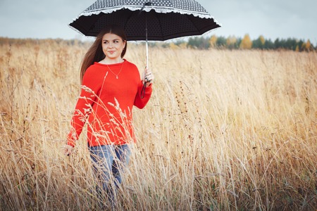 Beautiful girl in red dress in a yellow field in an autumn dayの写真素材