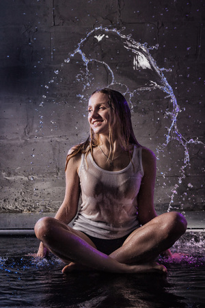 Girl in the white shirt with water drop in a dark room illuminated by light during a photoshoot with waterの写真素材