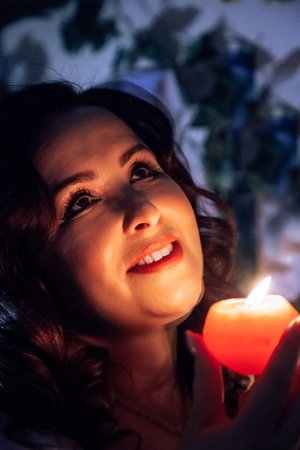 Portrait plump woman with black hair and red candle in her hand in the dark roomの写真素材