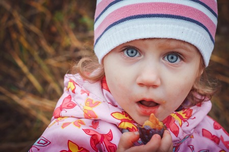 Portrait of a child of a little girl in a warm hat and warm clothes in an autumn day