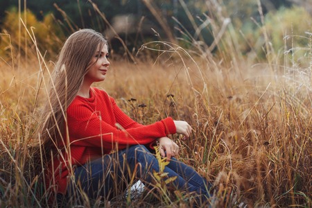 Beautiful girl in red dress in a yellow field in an autumn dayの写真素材