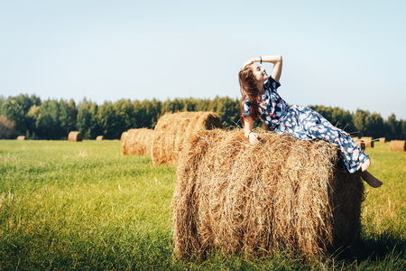 Teenager girl in a blue dress in an autumn field with hay stackの写真素材